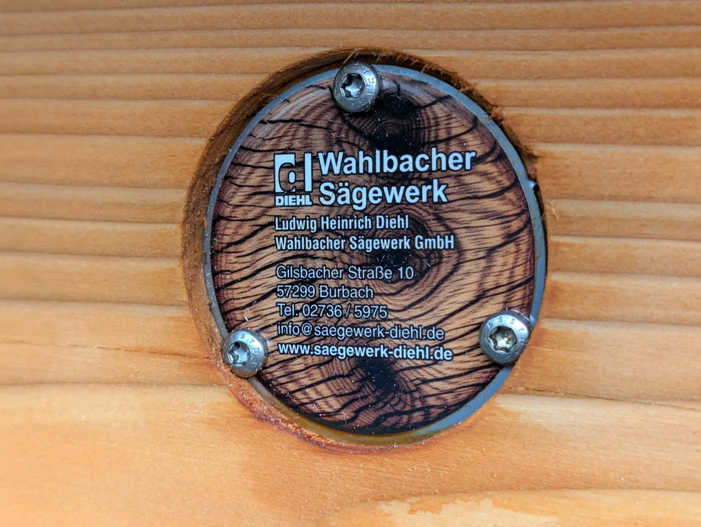 Rundes Schild des Sägewerks Diehl in Holzoptik, mit drei Schrauben in einen Holzbalken eingelassen